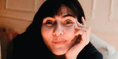 Person resting their face on their hand and looking at the camera indoors.