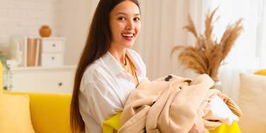 smiling woman putting her clean clothes on a chair in her bedroom