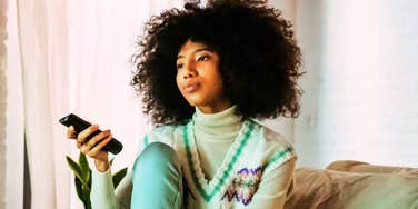 thoughtful woman sitting in her usual spot on the couch holding a remote