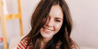 A smiling person with long brown hair wearing a striped shirt indoors