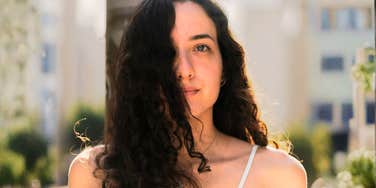thoughtful woman standing in warm sunlight with soft, serious expression and loose curls partially covering her face