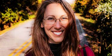 Close-up of a woman wearing glasses, smiling at the camera outdoors, conveying confidence and approachability.