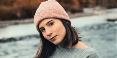 Woman outdoors wearing a grey sweater and pink beanie, head tilted, illustrating how communication style can influence attraction