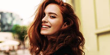 A woman smiling outdoors with long red hair.