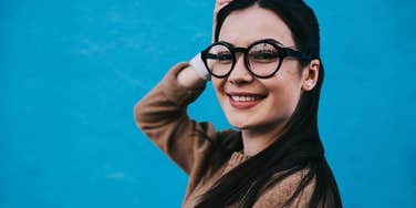 Deep thinking woman with glasses by a blue wall