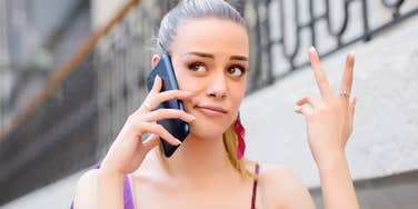 woman on phone with firm, unimpressed expression and subtle dismissive hand gesture, outdoor setting with blurred staircase background, conveying boundaries, frustration, and relationship disrespect.