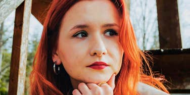 Person with red hair resting their chin on their hand outdoors