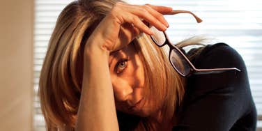 Woman taking off her glasses and resting her wrist on her head, showing signs of mental fatigue and overwhelm