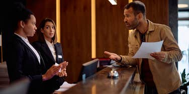 guest arguing with hotel workers behind desk