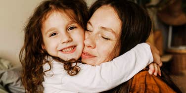 Mother hugging her young daughter, smiling, showing affection and support, emphasizing connection and life skills development.