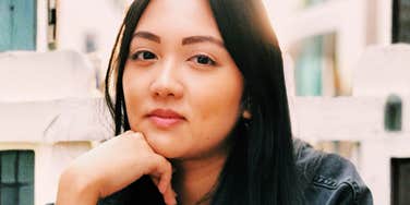 Person resting their chin on their hand while looking at the camera outdoors.