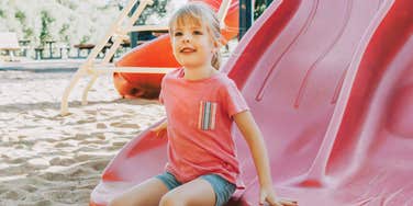 Little child at a park, having just slid down a slide, illustrating the structured and scheduled nature of modern kids’ friendships compared to past generations