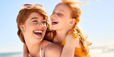 A mother and daughter laughing and having fun at the beach, representing the strong emotional bond and 'proactive parenting' needed to teach children the hard truths of friendship