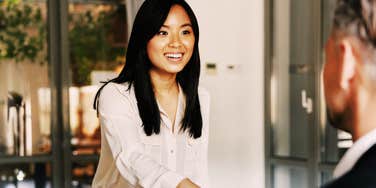A young Asian woman confidently shaking hands with two employers during a job interview, illustrating professional body language and interview techniques that help candidates succeed despite feeling nervous.