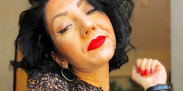 A confident woman with red lipstick and elegant jewelry looking matter-of-fact, representing the emotional well-being and sense of freedom that comes from finally moving on from a past relationship.