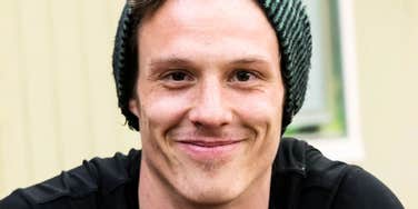 close-up of smiling young man wearing a dark beanie and black shirt, soft natural light, friendly expression, shallow depth of field background