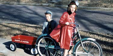 Children playing outside with a wagon and bike in the 1950s, capturing the active, self-directed childhood that experts link to long-term emotional resilience.