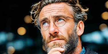A contemplative man in glasses reflecting on his daily habits, illustrating the mental clarity and happiness that come from letting go of negative behaviors and personal costs.