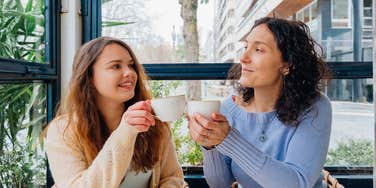 A Gen-X mother and her Gen-Z daughter smiling and talking over coffee, illustrating the 'shared values' and rare points of agreement between different generations.