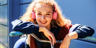 A young woman in Nineties-inspired sporty fashion posing with a vintage bicycle, capturing the nostalgic aesthetic of the era and the 'beauty mistakes' many grew up with.