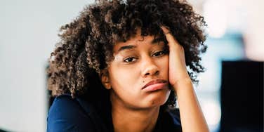 A unmotivated woman sitting at a table with her head in her hands, illustrating the 'internal resistance' and subconscious blocks that are often mistaken for laziness.