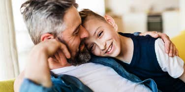 A happy father and son on a sofa, capturing the 'intentional parenting' rituals and supportive environment found in families who prioritize grit and capability.