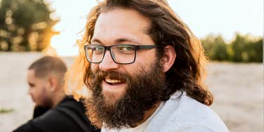 A smiling man with long hair and a beard at a beach bonfire with friends, illustrating the 'social battery' and personality traits of an introverted extrovert.