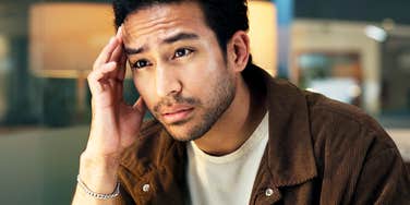 A man at his office desk with his hand on his head, illustrating the physical exhaustion and mental load associated with chronic workplace burnout triggers.