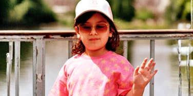 A young girl in a pink shirt and hat holding her hand up in a defiant gesture, illustrating the 'spoiled behavior' and boundary-testing experts address in modern parenting