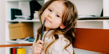Thoughtful child holding a black pencil to her chin, illustrating the simple life wisdom kids often know instinctively before adults relearn it later in life