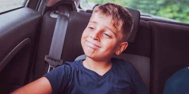 A happy young boy in a car seat, capturing the 'unfiltered joy' and high-spirited nature of raising boys and the long-term meaning behind the chaos.