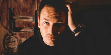 Man with a sinister glare rubbing his hand on his head, illustrating how narcissists may be drawn to religious communities, according to therapists