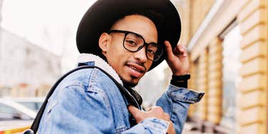 African man in trendy glasses and a denim jacket looking over his shoulder in a city setting, illustrating the mindset and small steps people take to bounce back after losing a job