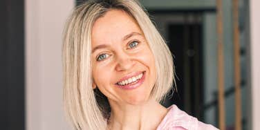 An attractive middle-aged woman smiling warmly at home, illustrating the 'low-effort' wellness habits and stress-reduction techniques that boost health in your fifties.