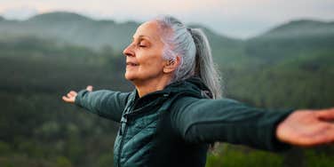A senior woman practicing deep breathing exercises in a foggy mountain setting, illustrating the 'vagus nerve' stimulation used to quiet a racing mind.