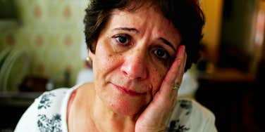 A woman in her sixties looking directly at the camera with a somber gaze, illustrating the deep emotional vulnerability and the lived experience of navigating loneliness.