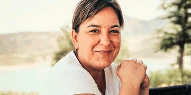 50-year-old woman smiling outdoors, representing genuine happiness and positive midlife transition.