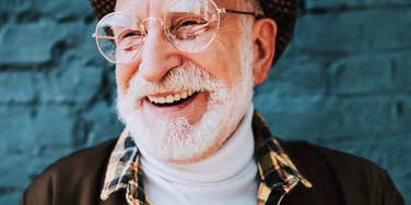 A cheerful pensioner smiling near a wall, illustrating the positive mindset and small daily habits that contribute to greater happiness as people grow older.