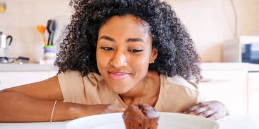 A Black woman thoughtfully looking at a sugary dessert, illustrating the 'delayed gratification' and cognitive reframing techniques used by people with high self-control.