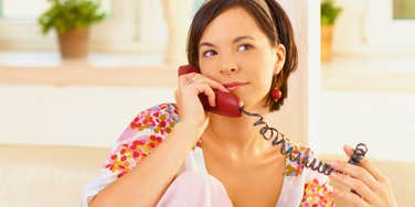woman using a landline phone smiling patiently