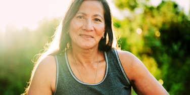A confident mature woman smiling radiantly outdoors, embodying the liberation and self-acceptance that comes from letting go of midlife insecurities.