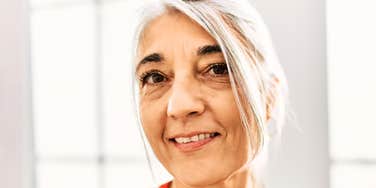 A smiling, gray-haired woman in her 60s, representing the authentic joy and timeless daily habits that contribute to a happy, fulfilling life.