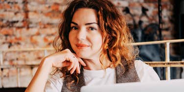 A confident young woman with curly red hair working on a laptop in a cafe, embodying the personality traits and focused mindset of a natural leader and modern entrepreneur.