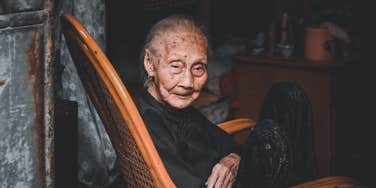 An elderly woman sitting thoughtfully on a wooden chair, illustrating the 'life review' process and the common regrets experts hear at the end of life.