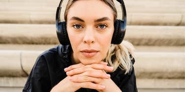 A young blonde woman sitting on stairs with headphones on, illustrating the 'internal focus' and mindfulness needed to listen to your gut instincts.