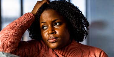 Portrait of a stressed woman contemplating on a couch, capturing the internal strain and bodily 'price' paid by living in a state of constant high-alert anxiety.