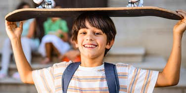 young boy holding a skateboard to use after school