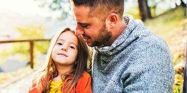 A father looking at his young daughter with a mix of pride and realization as she stands confidently outdoors, illustrating the moment parenting theory meets real-world growth.