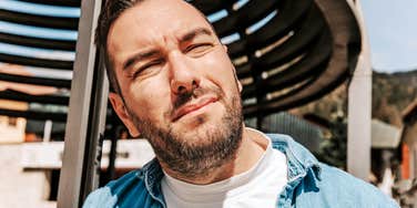 A handsome millennial man with a perplexed, squinting expression, illustrating the common emotional fatigue and uncertainty associated with the modern 'struggling millennial' experience.