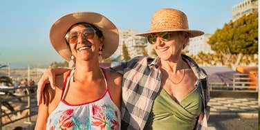 Two women in their fifties laughing together while walking along the beach, illustrating small daily habits that support happiness in your fifties and sixties